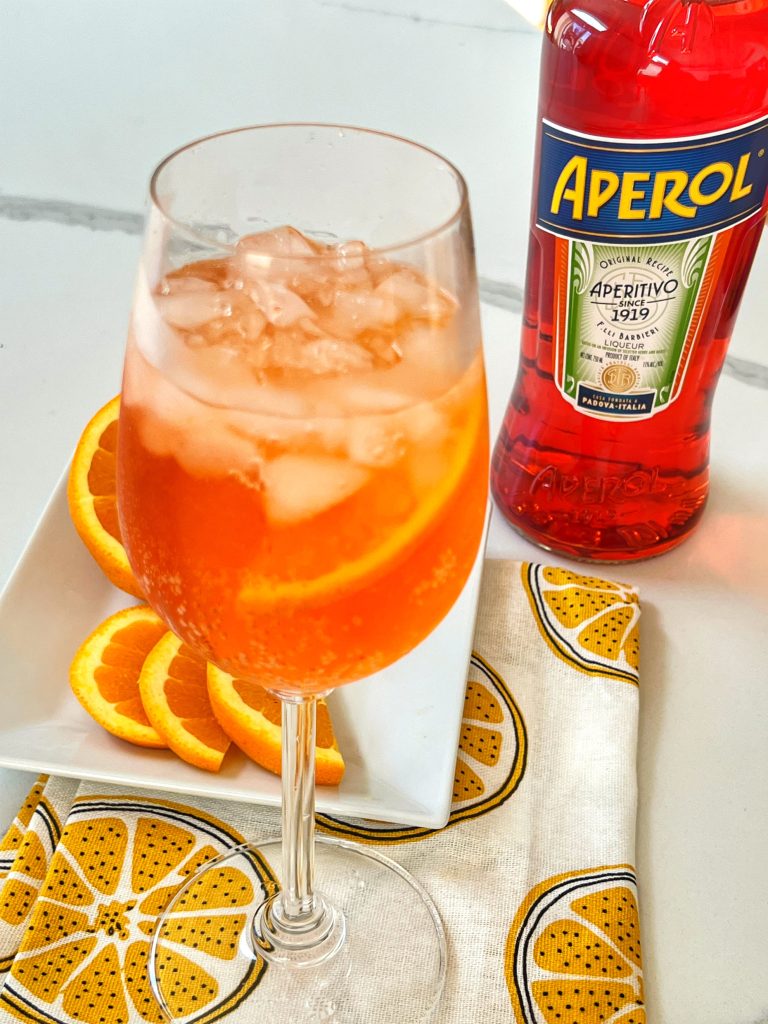 An Aperol Spritz is an adult beverage that is a the perfect refreshing summer drink. It's a mixture of Prosecco (or bubbly wine), Aperol and a splash of sparkling water. It's low in alcohol and really popular in Northern Italy, where it's considered an Aperitif. The flavor has a hint of orange and herbs and is a perfect beverage to enjoy "Al Fresco". 