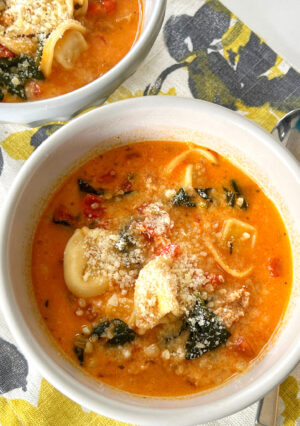 A bowl of hearty tortellini soup with spinach.