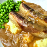 A plate of sausages with onion gravy and mashed potatoes.