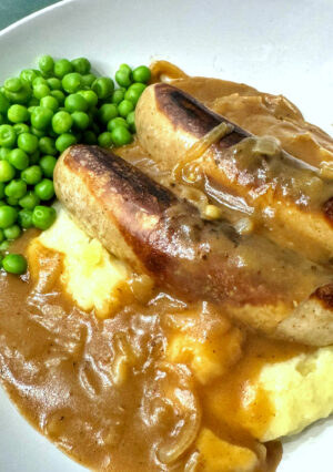 A plate of sausages with onion gravy and mashed potatoes.