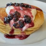 A stack of whole wheat pancakes topped with sweetened yogurt and blueberries.