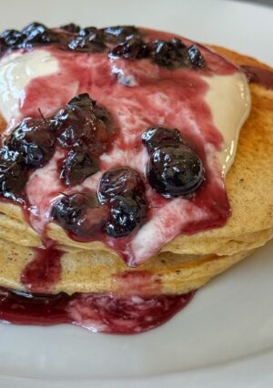 A stack of whole wheat pancakes topped with sweetened yogurt and blueberries.