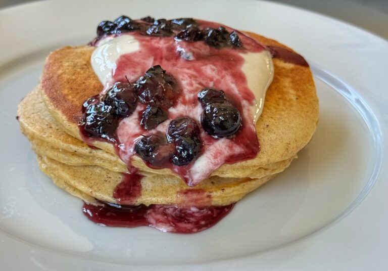 A stack of whole wheat pancakes topped with sweetened yogurt and blueberries.