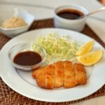 A plate of breaded pork cutlets with cabbage and a special sauce.