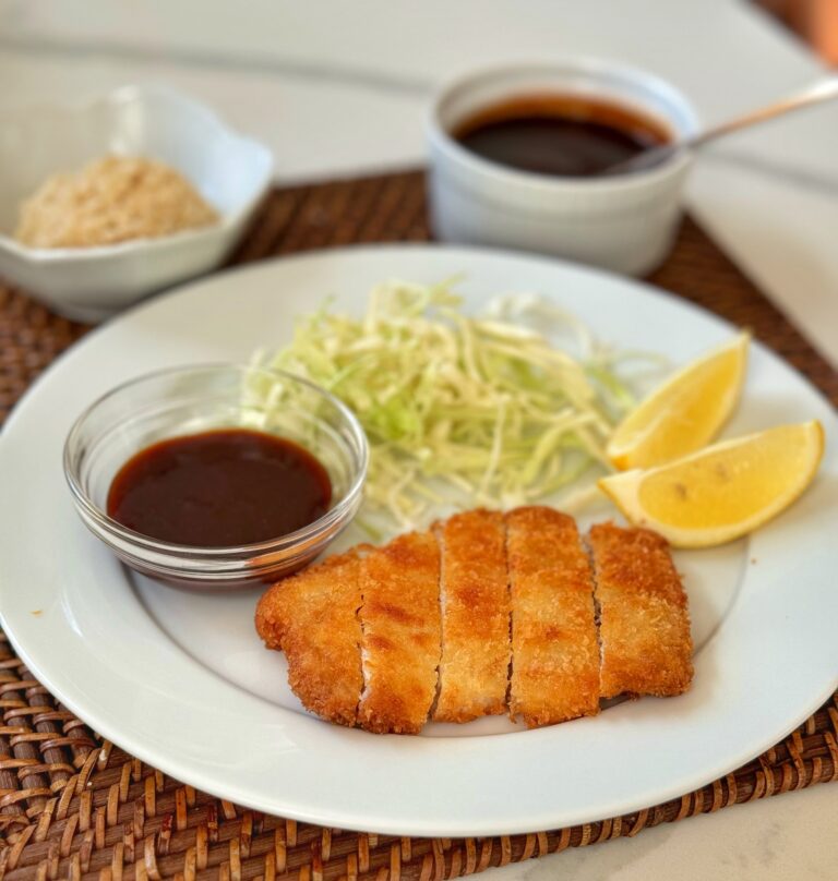 A plate of breaded pork cutlets with cabbage and a special sauce.